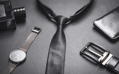 Tie with a wristwatch and perfume on the black background. Men accessories