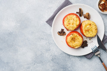 Baked whole tomatoes stuffed with mushrooms and cheese with spices on a light concrete background. Copy space.