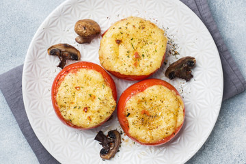 Baked whole tomatoes stuffed with mushrooms and cheese with spices on a light concrete background.