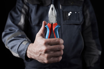 Professional worker in overalls shows pliers on a dark background