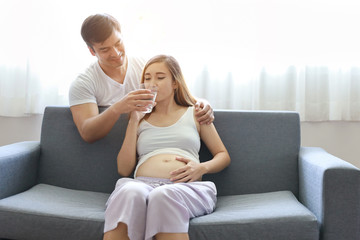 medium shot of young caucasian husband embracing young asian pregnant belly wife with happiness and...