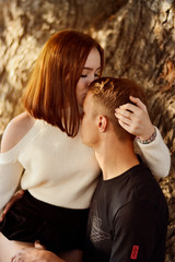 A beautiful girl sits on the lap of a young guy and kisses him on the forehead 