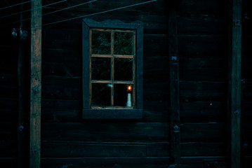 Halloween horror building. Reflection and shadows of a spooky tree in the window of an old wooden dark mystical ghostly house in the forest and the light from a lamp in night darkness