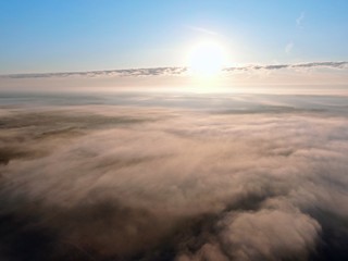 Aerial view of drone flight above clouds at dawn with fog.
