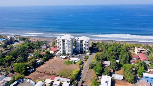Aerial: Two White Beachfront Hotels Towering Over Sand With City and Mountains in the Background - Jaco, Costa Rica