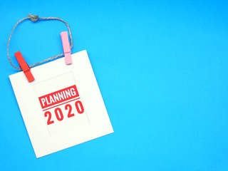 Top view of white frame paper with word "Planning 2020" rope and wood clip on blue table. Happy new year, Plan the future. Copy space for any text design.