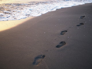 foot prints on a black sand beach with tilt-shift blur. Surf in background. Concept for loneliness, solitude, depression