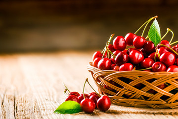 Cherry in wooden basket with leaves on table. Detail or close up of cherries  and copy space.