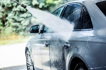 Washing a car using high pressure water spray or jet from side. Luxury vehicle cleaning in summer time.