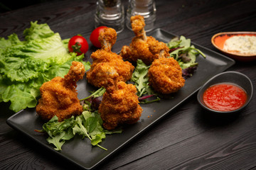 breaded chicken wings with spicy sauce and herbs on a black board