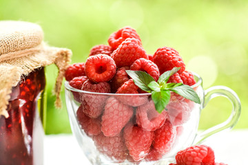 Fresh beautiful raspberry in glass cup on white table. Jam or marmelade homemade from raspberries in glasss bottle.