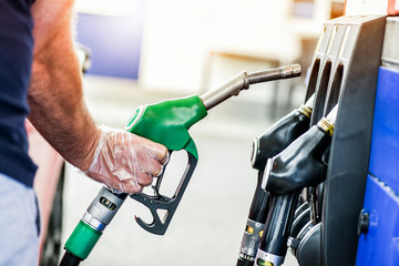 Man after refueling gasoline at gas station. Hand with clear gloves put fuel pump or pistol into...