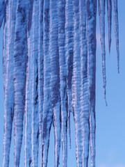 Ice icicles hanging from roof of house. Window covered with large and dangerous, but beautiful transparent icicles. Blue sky with clouds background.