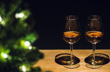 Two glasses of Rose wine on wooden table with Christmas tree and dark background.