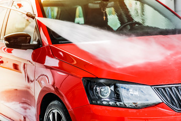 Water jet or high pressure car washing. Manual spray cleaning of red vehicle close up or detail.