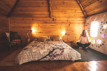 Alternative relaxed caucasian woman meditating and relaxing at home in yoga balance position -  artistic wall with coloured glass and wood wall in background