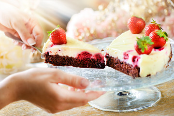 Finest chocolate tart with vanilla cream, strawberries topped. Woman hands serving cake or dessert dish on glass tray.