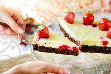 Finest chocolate tart with vanilla cream, strawberries topped. Woman hands serving cake or dessert dish on glass tray.