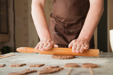 Men's hands and dough close-up. Baking gingerbread Christmas and Easter gingerbread cookies. A man in the kitchen is preparing cookies in an apron and copy space.