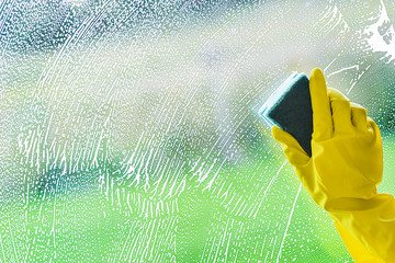 Woman hand in yellow gloves cleaning windows with sponge and spray. Washing house concept. Smudges or smears on clear glass.