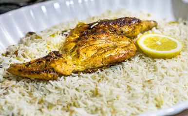 top view of delicious tasty chicken barbecued on the top of white rice and green fresh lemon slices in a white plate 