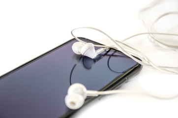 black phone and white headphones on a white background. Close-up.