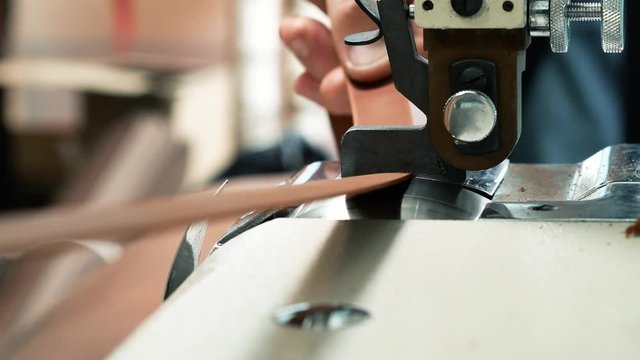 Craftsman using an automatic leather skiving machine. Skiving leather belt in a haberdashery manufactory. Splitting, aligning and cutting edge of leather details 4k