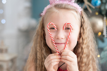 girl 5 years old with sweet lollipop candy cane near christmas tree.