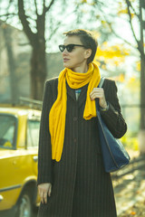 Beautiful autumn woman wearing trendy sunglasses, coat, yellow scarf in the street with yellow car...