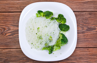 Cellophane noodles with broccoli in a white plate on wooden background.