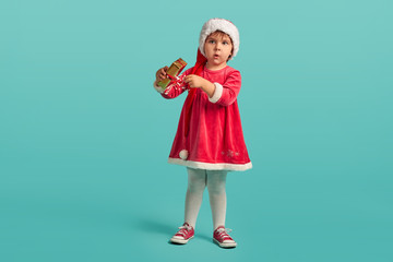 Adorable small baby girl in christmas hat and red dress on the studio background