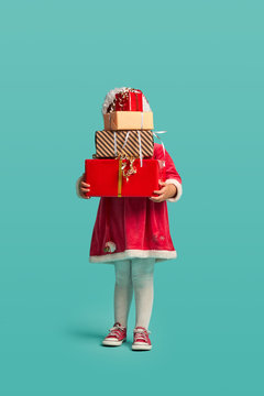 Adorable Small Baby Girl With Present Box In Christmas Hat And Red Dress On The Studio Background