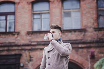 portrait of a young businessman in a coat walking around the city with coffee