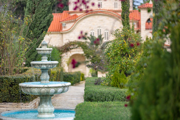 Naklejka premium White three-tiered fountain with azure interior paint in the middle of the garden.
