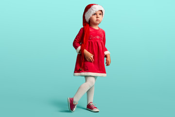 Adorable small baby girl in christmas hat and red dress on the studio background