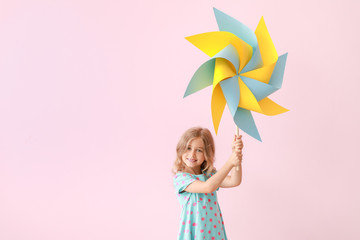 Cute little girl with paper windmill on color background