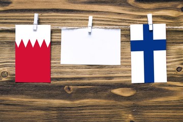 Hanging flags of Bahrain and Finland attached to rope with clothes pins with copy space on white note paper on wooden background.Diplomatic relations between countries.