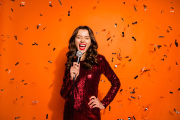 Portrait of charming bachelor girl have prom party event sing song hold microphone feel fun wear luxury chic clothing isolated over orange color background serpentine falling