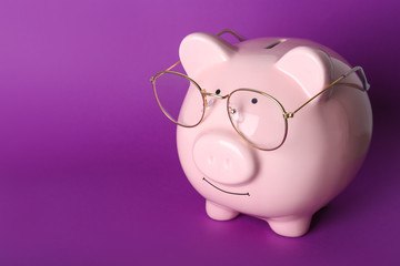 Piggy bank with eyeglasses on color background