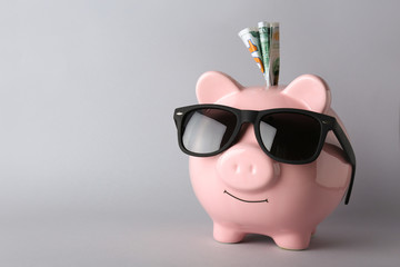 Piggy bank with sunglasses and money on grey background