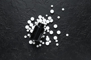 Jar and many scattered pills on dark background