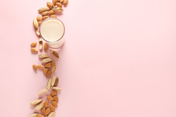 Glass of tasty almond milk and nuts on color background