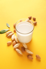 Glass of tasty almond milk on color background