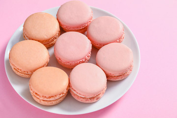Plate with tasty macarons on color background