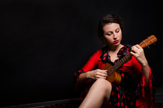 Carmen beautiful woman in red dress, with guitar on dark background sitting on the floor