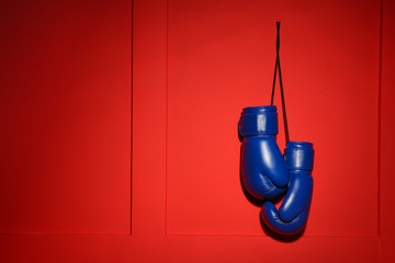 Pair of boxing gloves hanging on color wall