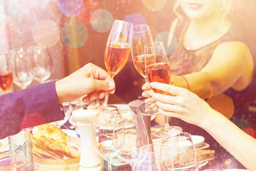 Clinking glasses of champagne in hands on bright lights background with snow effect