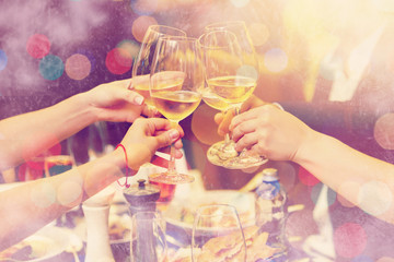 Clinking glasses of champagne in hands on bright lights background with snow effect