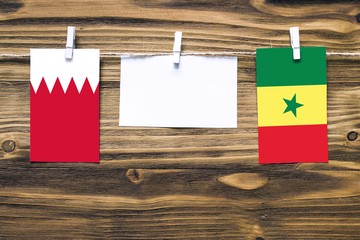 Hanging flags of Bahrain and Senegal attached to rope with clothes pins with copy space on white note paper on wooden background.Diplomatic relations between countries.