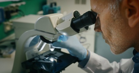 Portrait of a male scientist is analyzing a sample to extract the DNA and molecules with microscope in laboratory.